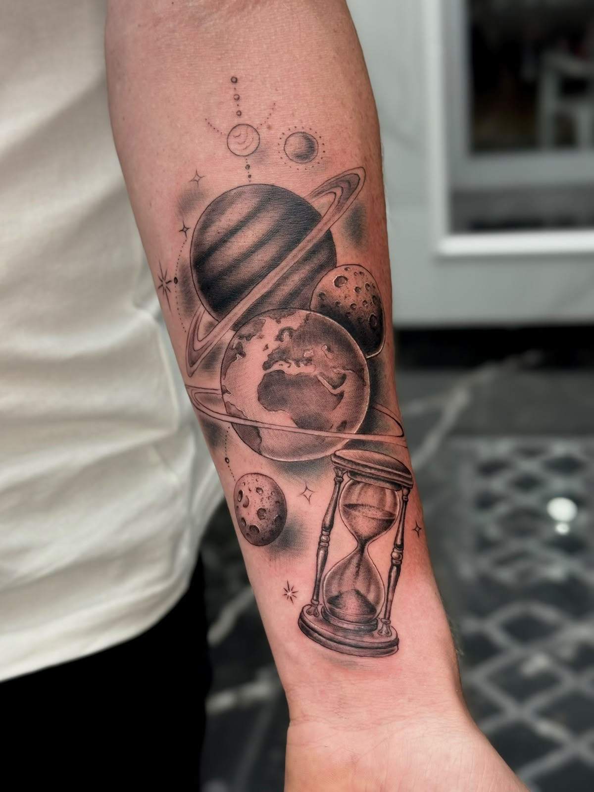 Fine line space tattoo with planets, Earth and hourglass by Christos at Black Sheep Tattoo Studio in Kos